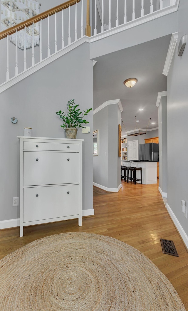 entrance foyer with light hardwood / wood-style flooring, a high ceiling, and ornamental molding