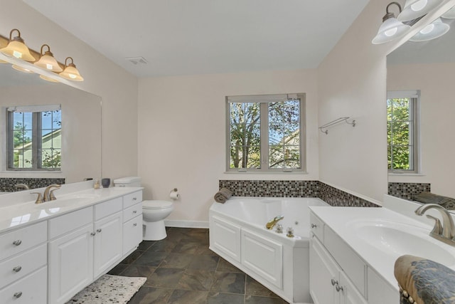 bathroom with vanity, a tub to relax in, toilet, and a healthy amount of sunlight