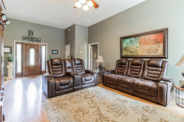 living room with ceiling fan, light wood-type flooring, and a towering ceiling