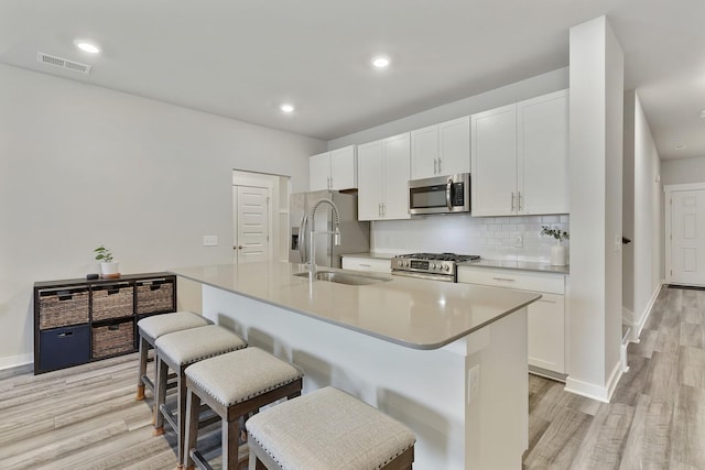 kitchen with white cabinets, a kitchen island with sink, appliances with stainless steel finishes, and a kitchen bar