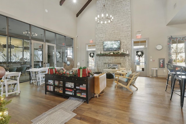 living room with a high ceiling, wood-type flooring, beamed ceiling, an inviting chandelier, and a large fireplace