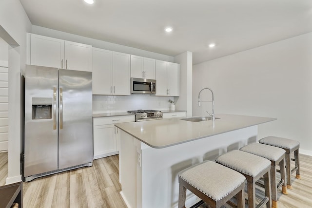 kitchen featuring appliances with stainless steel finishes, decorative backsplash, sink, white cabinets, and a center island with sink