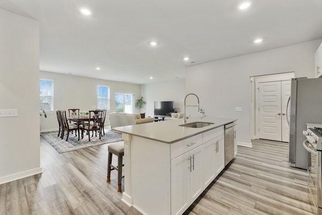 kitchen with light hardwood / wood-style flooring, sink, white cabinetry, a center island with sink, and stainless steel appliances