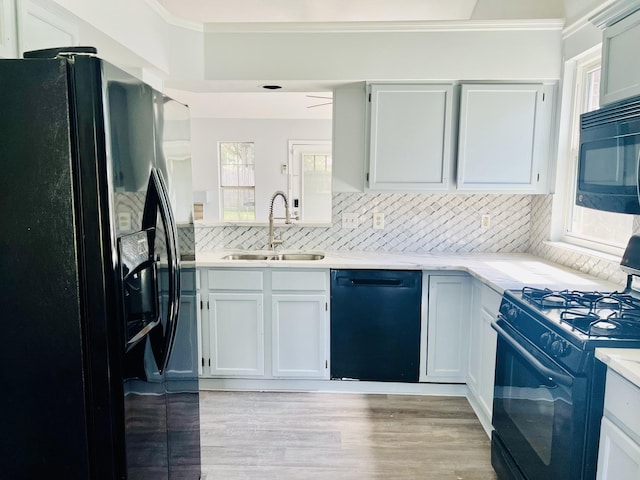 kitchen with a healthy amount of sunlight, white cabinets, black appliances, and light wood-type flooring