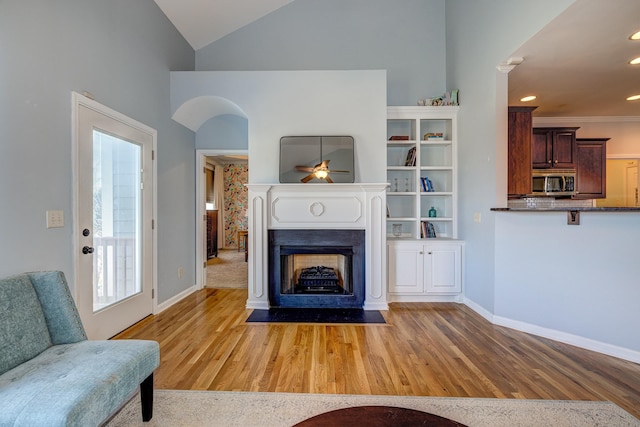 living room with ceiling fan, crown molding, high vaulted ceiling, and light hardwood / wood-style floors