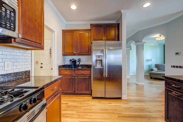 kitchen featuring dark stone countertops, ornamental molding, light hardwood / wood-style floors, and appliances with stainless steel finishes