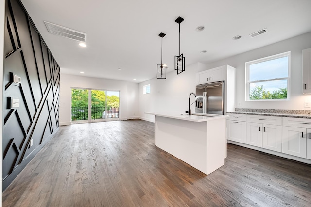 kitchen featuring stainless steel fridge, dark wood-type flooring, white cabinets, and an island with sink