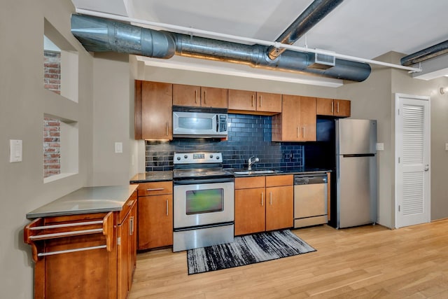 kitchen featuring light wood-type flooring, stainless steel appliances, backsplash, and sink