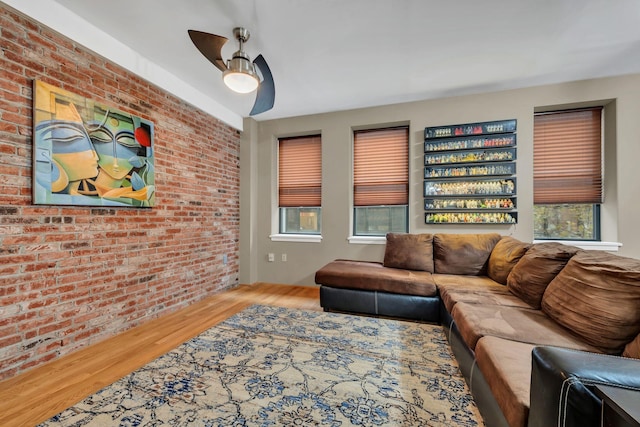 living room featuring ceiling fan, wood-type flooring, and brick wall