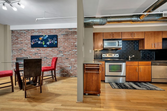 kitchen with tasteful backsplash, brick wall, stainless steel appliances, sink, and light hardwood / wood-style floors