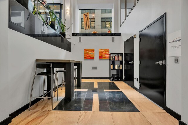 hall with tile patterned flooring and a towering ceiling