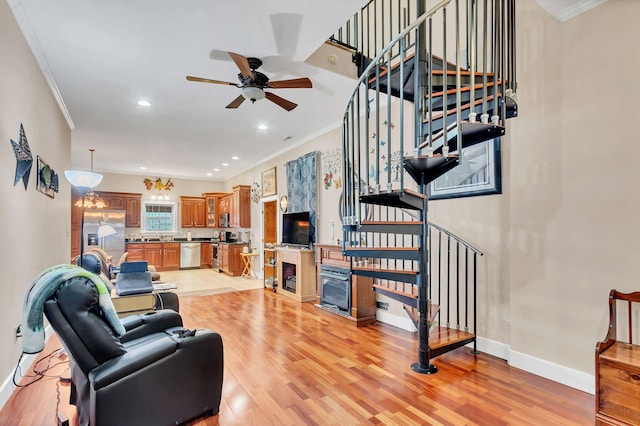 living room featuring ceiling fan with notable chandelier, light wood-type flooring, and crown molding