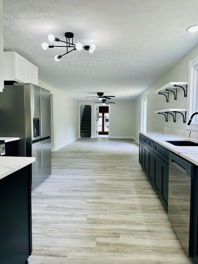 kitchen featuring sink, stainless steel appliances, light stone counters, a textured ceiling, and light wood-type flooring