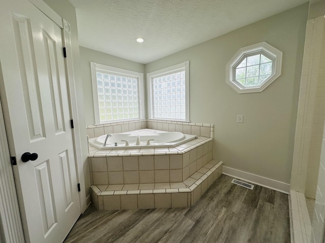 bathroom with a relaxing tiled tub, a textured ceiling, and hardwood / wood-style flooring