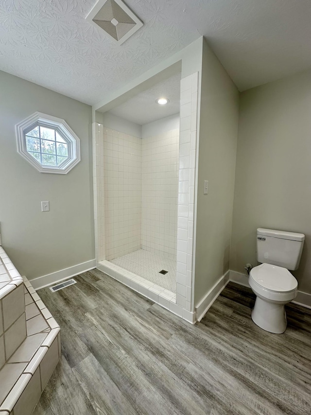 bathroom featuring toilet, a tile shower, wood-type flooring, and a textured ceiling