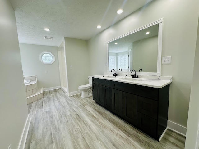 bathroom featuring a bathtub, vanity, toilet, a textured ceiling, and wood-type flooring