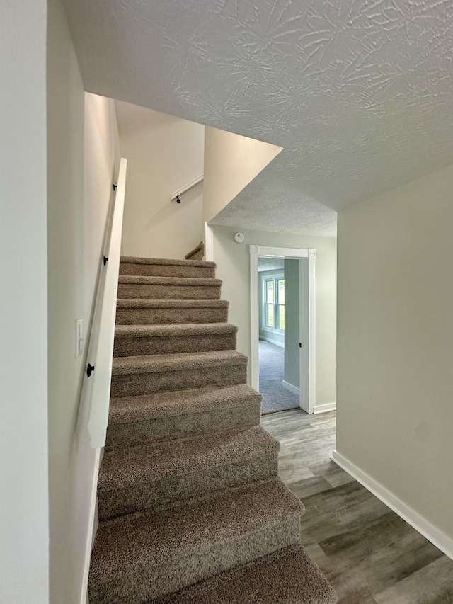 staircase with hardwood / wood-style floors and a textured ceiling