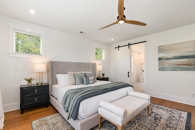 bedroom with a barn door, light hardwood / wood-style floors, ceiling fan, and ensuite bathroom