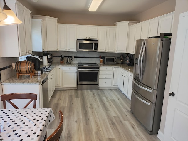 kitchen with white cabinets, appliances with stainless steel finishes, light wood-type flooring, and tasteful backsplash