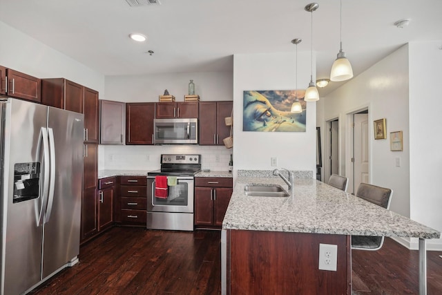 kitchen with kitchen peninsula, appliances with stainless steel finishes, a kitchen bar, dark hardwood / wood-style flooring, and sink