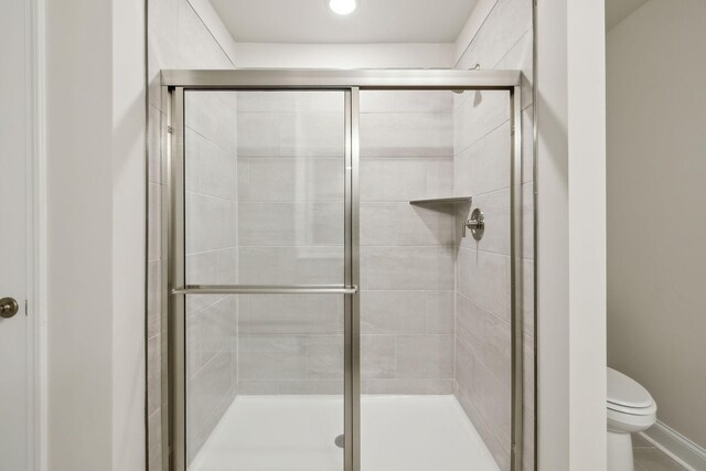 bathroom featuring tile patterned flooring, toilet, and a shower with door