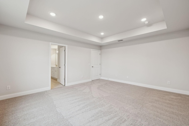 spare room with a tray ceiling and light carpet