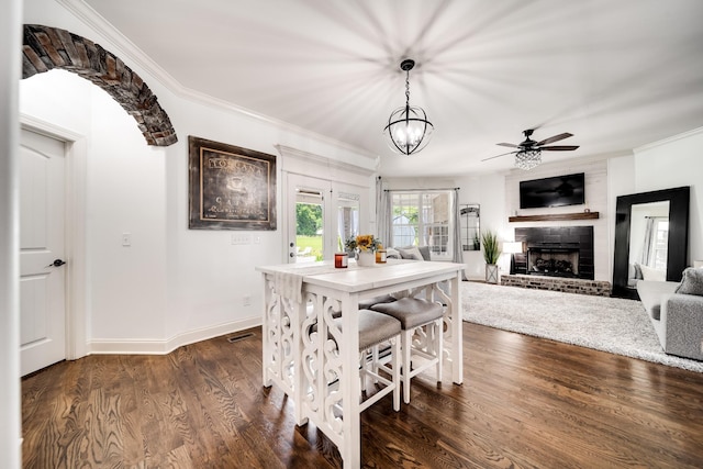 dining room featuring a fireplace, dark hardwood / wood-style flooring, ceiling fan with notable chandelier, and crown molding