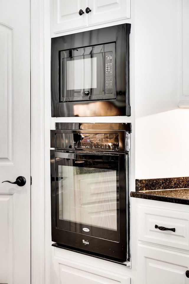 interior space with dark stone countertops, white cabinetry, and black appliances