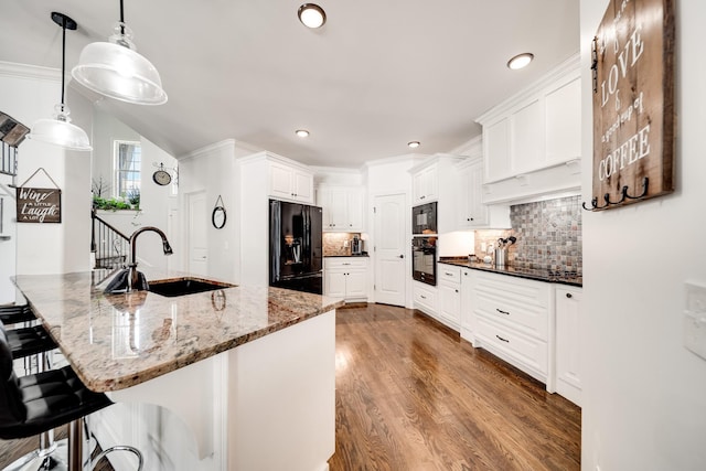 kitchen with sink, dark stone countertops, pendant lighting, black appliances, and hardwood / wood-style flooring