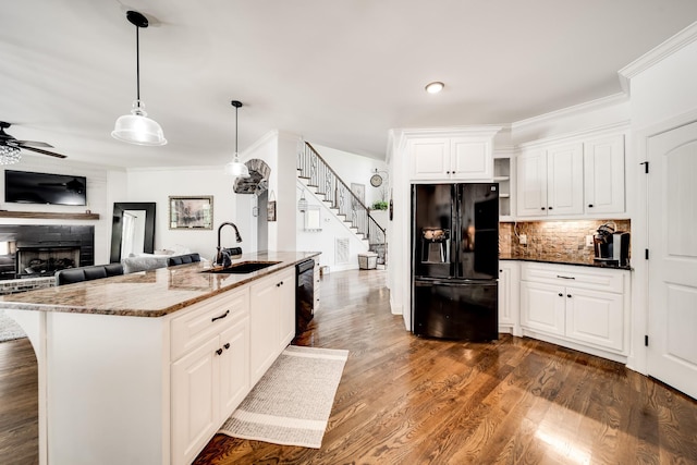 kitchen with dark hardwood / wood-style flooring, dark stone counters, sink, black appliances, and a center island with sink