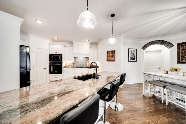 kitchen featuring light stone counters, sink, black appliances, pendant lighting, and white cabinetry