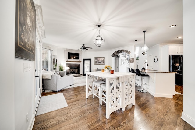 dining room featuring crown molding, ceiling fan, a large fireplace, and dark wood-type flooring