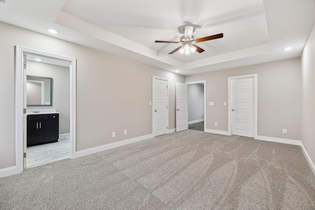 unfurnished bedroom featuring ensuite bath, ceiling fan, light carpet, and a tray ceiling