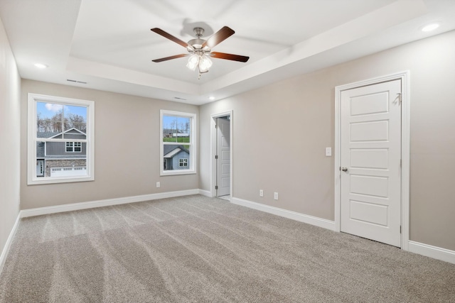 carpeted empty room with a raised ceiling and ceiling fan