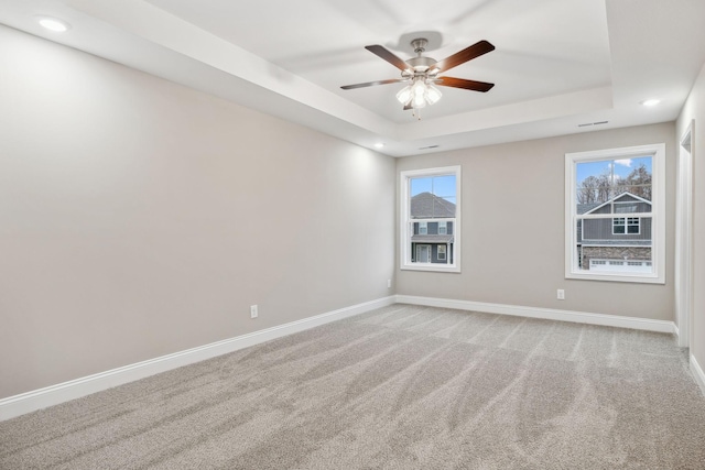 carpeted spare room featuring ceiling fan and a raised ceiling