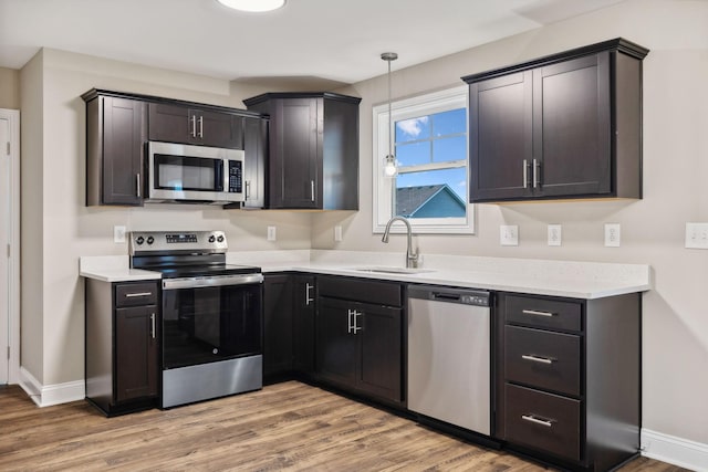 kitchen with dark brown cabinets, stainless steel appliances, sink, wood-type flooring, and pendant lighting