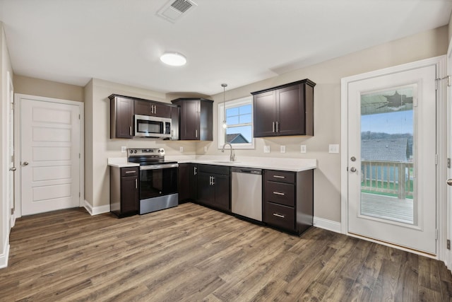 kitchen with appliances with stainless steel finishes, dark hardwood / wood-style flooring, dark brown cabinetry, sink, and pendant lighting