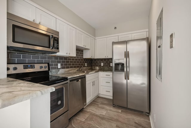 kitchen with light stone countertops, appliances with stainless steel finishes, tasteful backsplash, sink, and white cabinetry