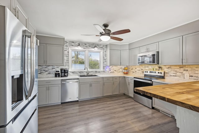 kitchen with sink, stainless steel appliances, butcher block countertops, backsplash, and light hardwood / wood-style floors