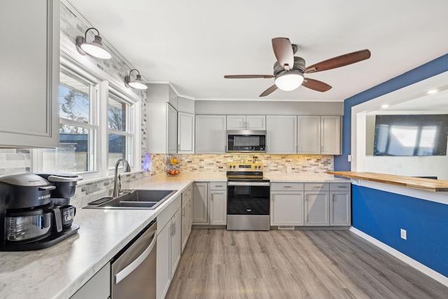 kitchen featuring gray cabinetry, backsplash, sink, light hardwood / wood-style flooring, and appliances with stainless steel finishes