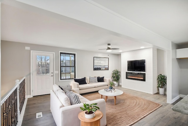 living room with a large fireplace, hardwood / wood-style flooring, and ceiling fan