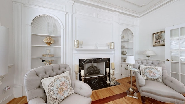 sitting room with built in shelves, a premium fireplace, light hardwood / wood-style floors, and ornamental molding