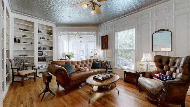 sitting room featuring built in shelves, a textured ceiling, ceiling fan, crown molding, and light hardwood / wood-style flooring