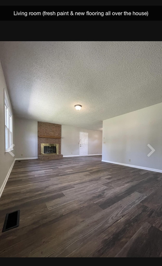 unfurnished living room with dark wood-type flooring, a textured ceiling, and a brick fireplace