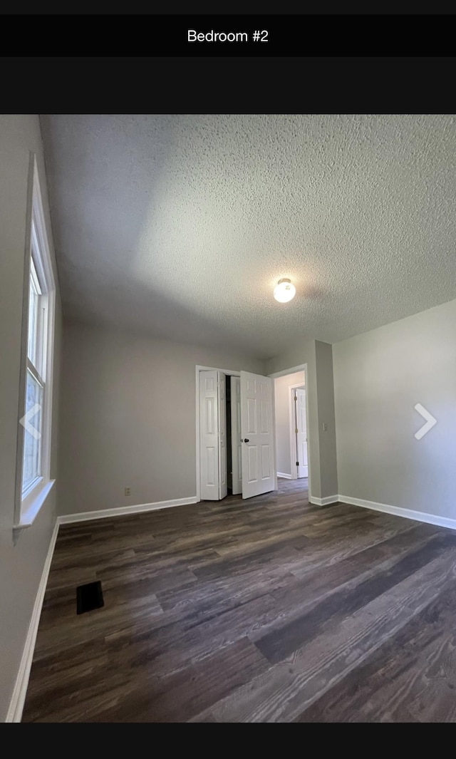 empty room with a textured ceiling and dark hardwood / wood-style floors