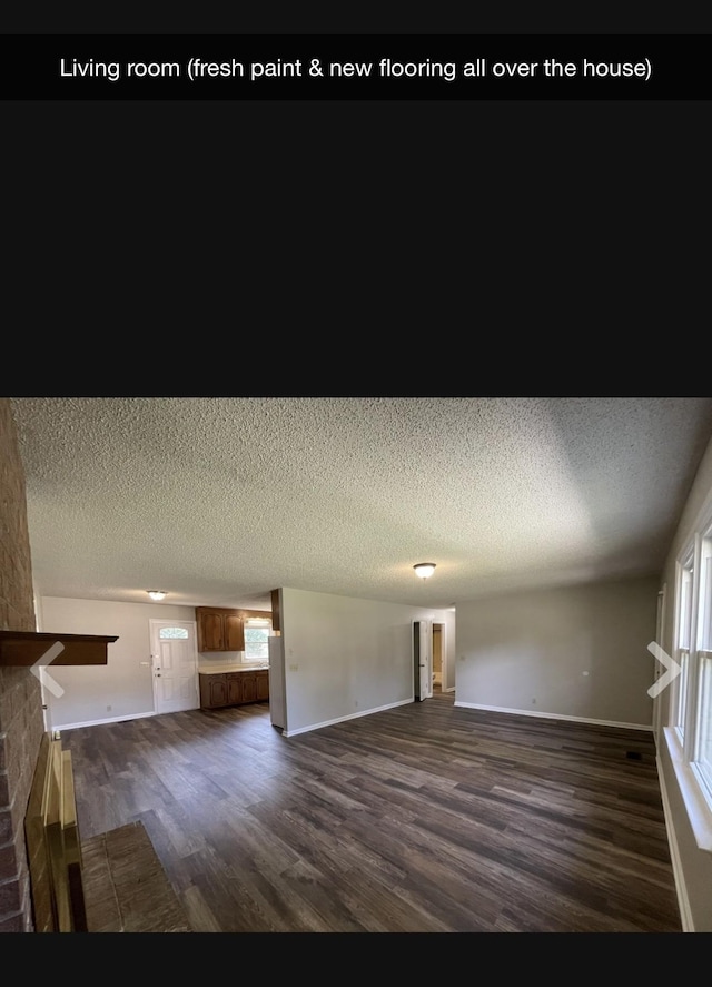 unfurnished living room featuring dark wood-type flooring, a textured ceiling, and a brick fireplace