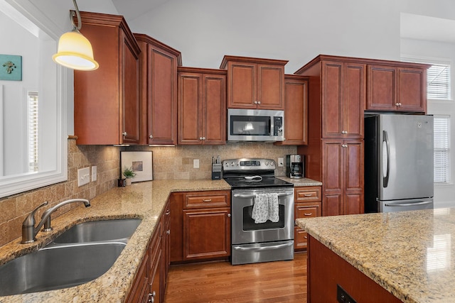 kitchen with sink, stainless steel appliances, tasteful backsplash, pendant lighting, and light wood-type flooring