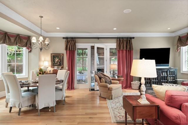 living room with a notable chandelier, crown molding, a wealth of natural light, and light hardwood / wood-style flooring