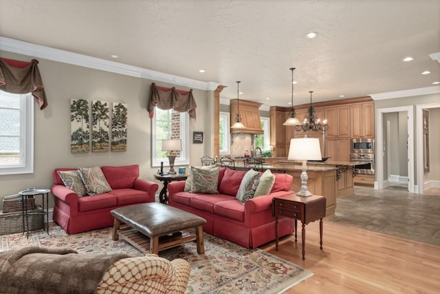 living room with a notable chandelier, sink, crown molding, and light hardwood / wood-style flooring