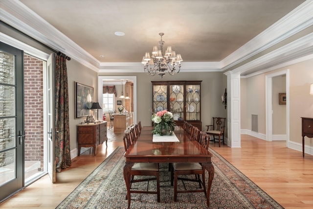 dining room featuring decorative columns, crown molding, light hardwood / wood-style floors, and a notable chandelier